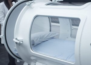 Close up of a hyperbaric oxygen therapy chamber. Through the window of the chamber, we see a cozy, comfortable surface with a pillow.